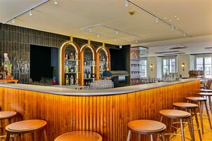 Una zona de bar moderna con una barra de madera, taburetes y estantes llenos de botellas.