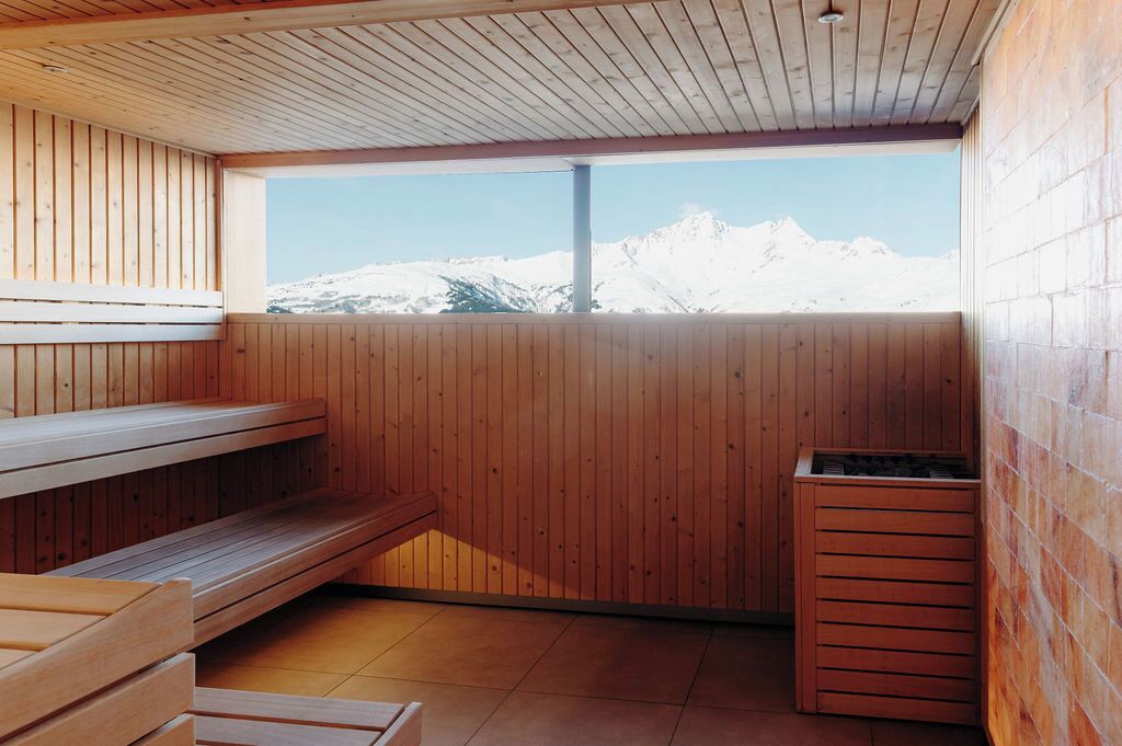 A sauna room with wooden benches and a window overlooking snow-capped mountains.