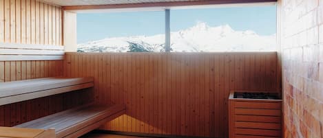 A sauna room with wooden benches and a window overlooking snow-capped mountains.