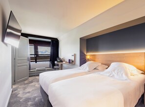 Habitación de hotel con dos camas, un escritorio, una silla, un televisor y ventana con vistas.