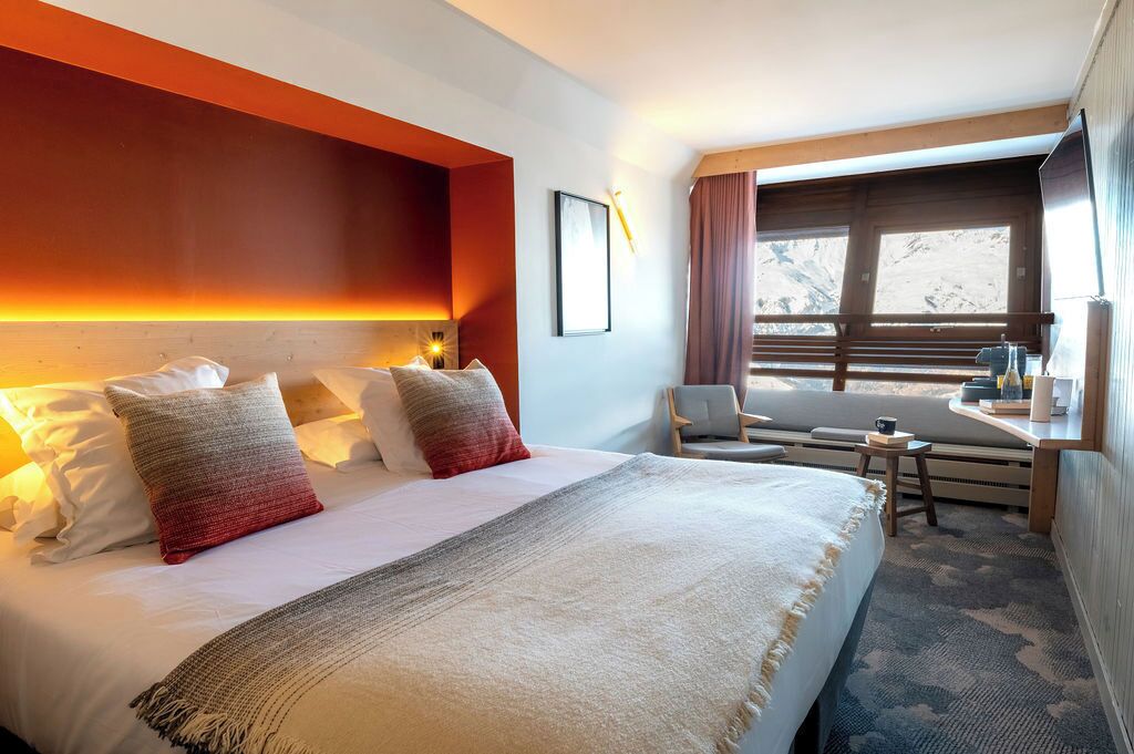 Une chambre d’hôtel avec un grand lit, un bureau avec une chaise et une fenêtre avec des rideaux.