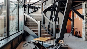 Un interior moderno con una escalera, una zona de estar con sofá y mesas, y ventanas amplias.