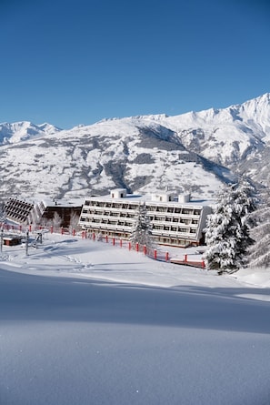 Un hotel cubierto de nieve con un diseño arquitectónico moderno, con varios pisos y una pista de esquí al fondo.