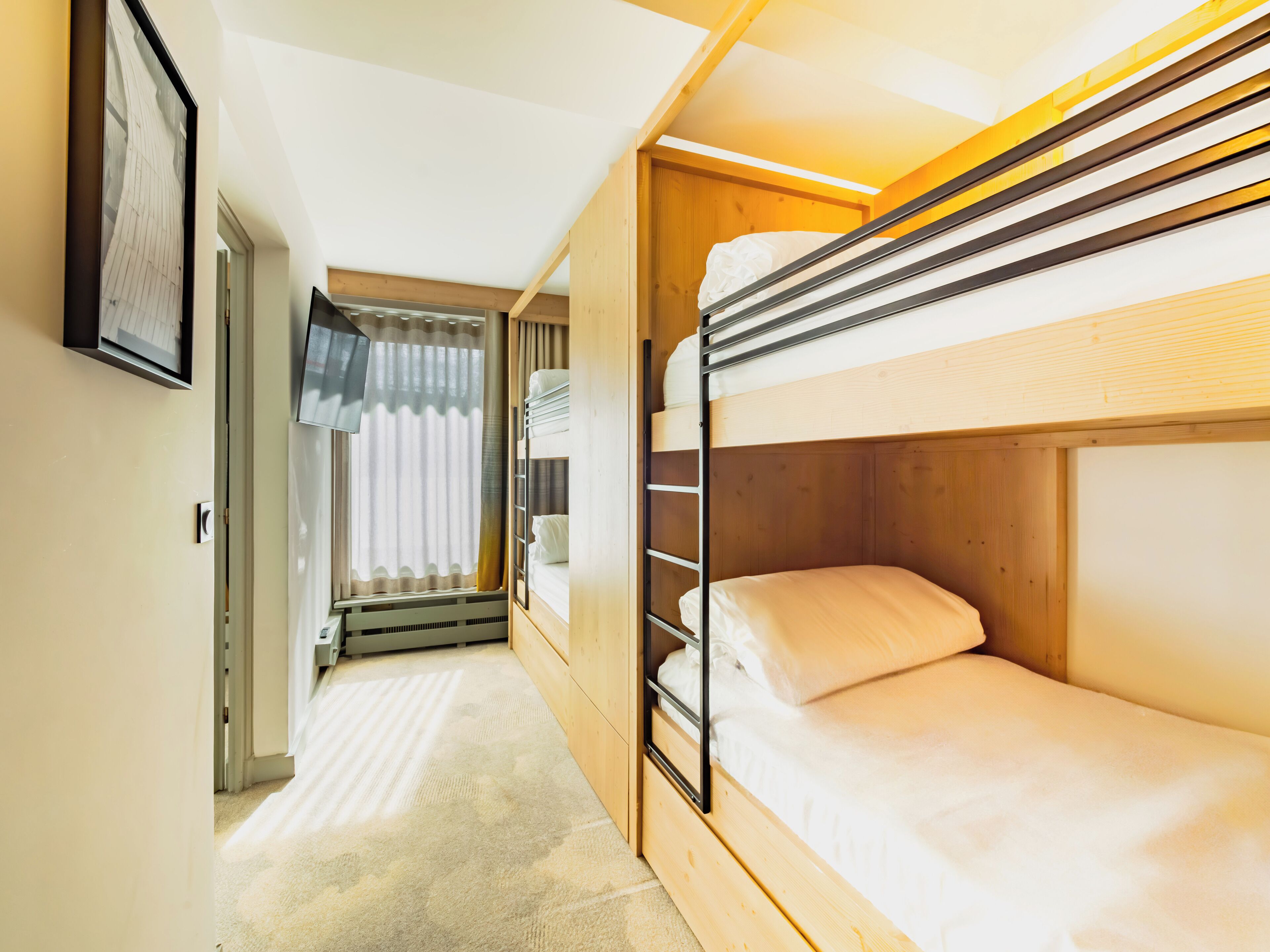 Une chambre avec un lit superposé, une fenêtre, un radiateur et une porte donnant sur une autre pièce.