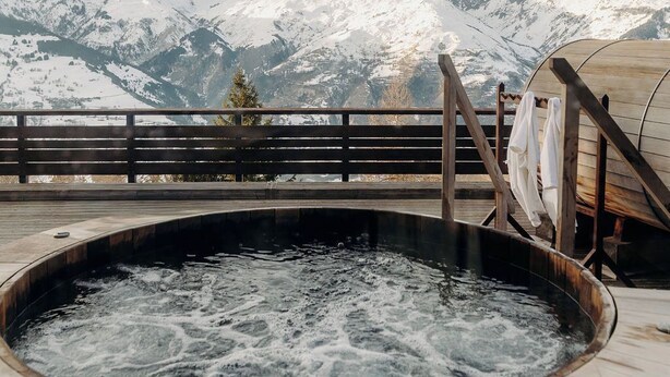 Un jacuzzi con terraza y baranda de madera, con vistas a montañas nevadas.