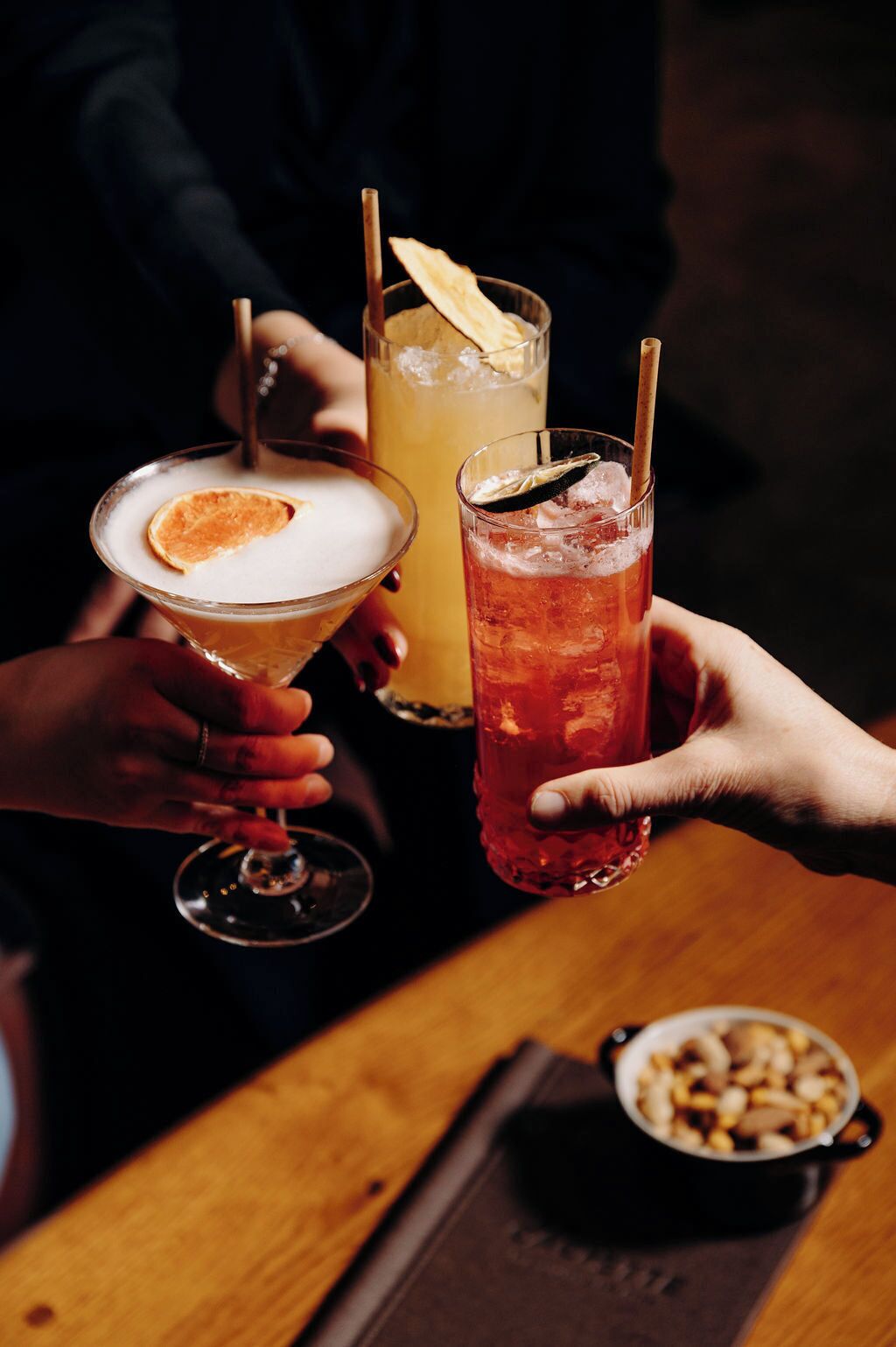 Tres personas sosteniendo bebidas en una mesa con un cuenco de nueces.