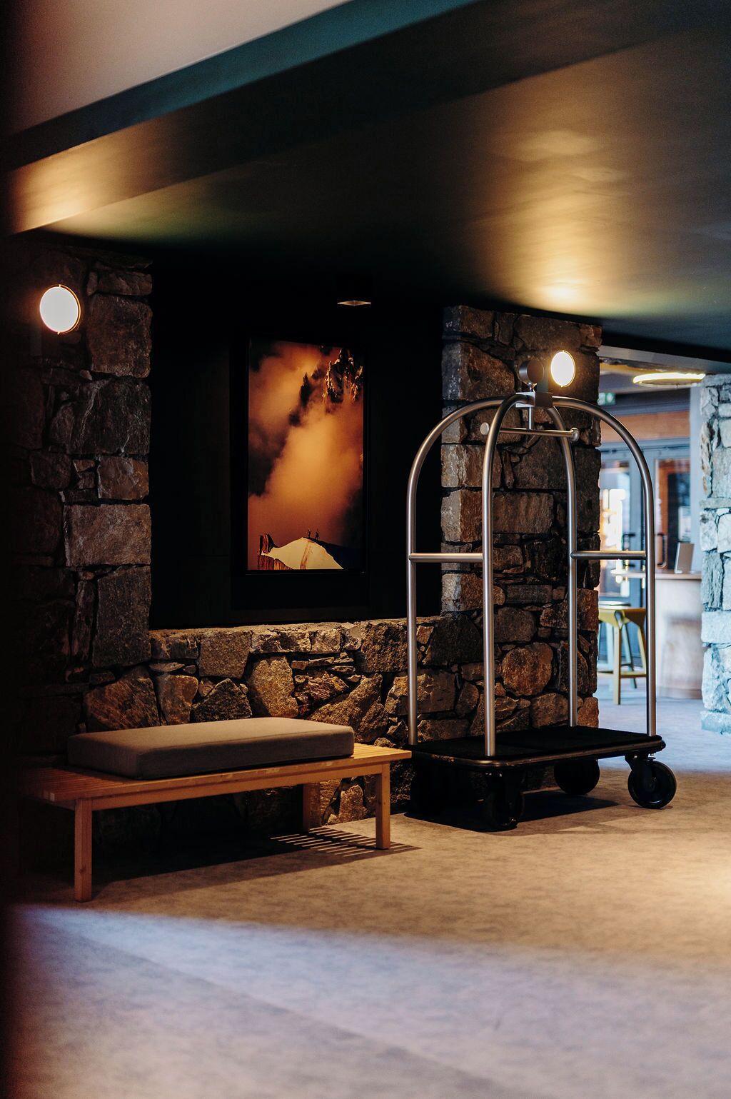 A lobby with a stone wall, a bench, a cart, and a framed picture of a mountain.