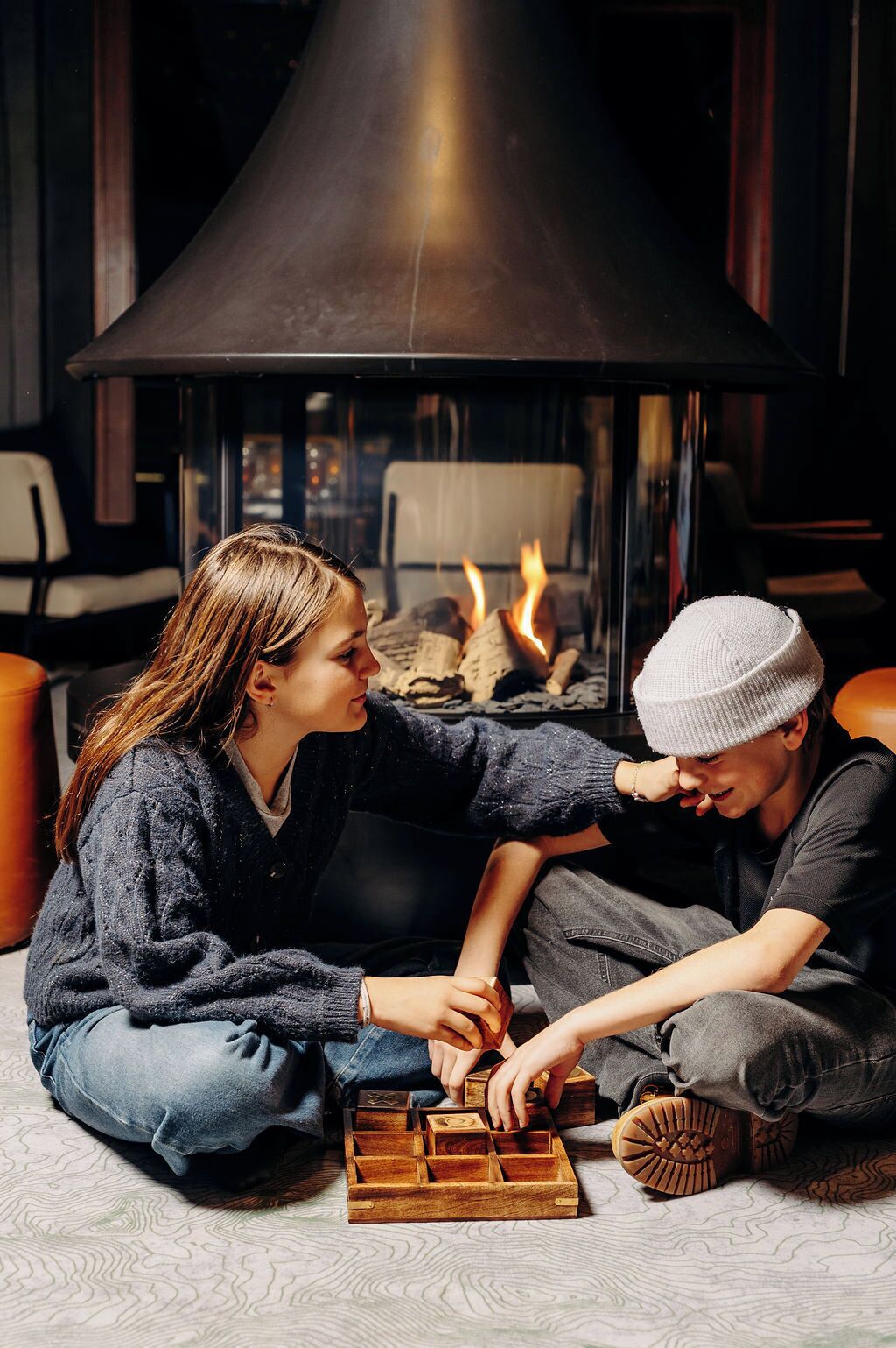 Due persone sedute sul pavimento che giocano a un gioco di puzzle di legno vicino a un caminetto.
