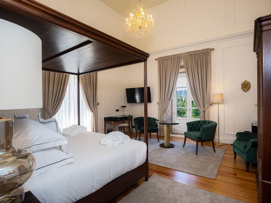 Una cama con dosel, un televisor y un escritorio al fondo, un candelabro y vistas al exterior.
