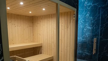 A sauna with wooden benches and a glass door, set against a dark marble wall.
