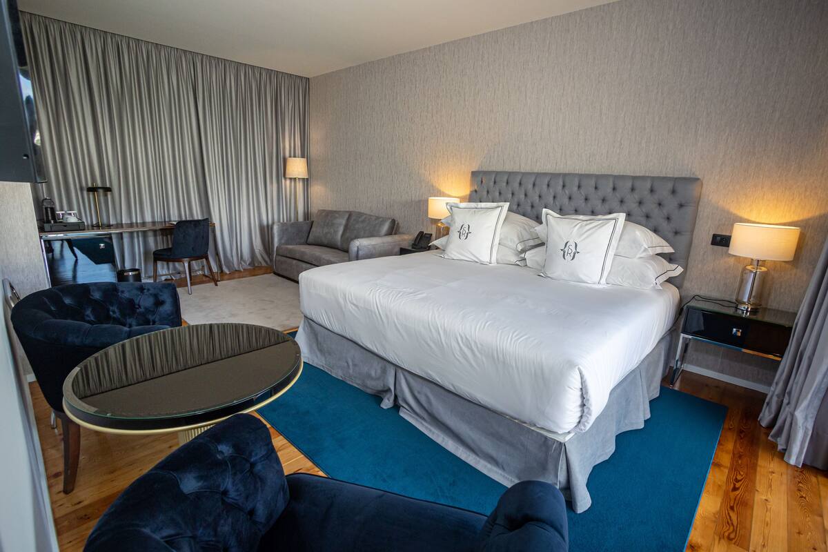 A hotel room with a large bed, two armchairs, a small table, a desk, and a chair.