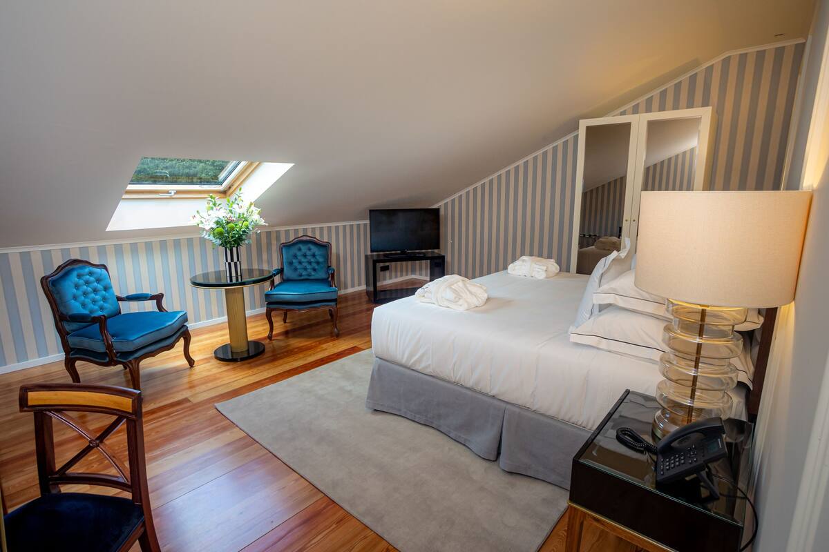 A bedroom with a bed, a TV, a chair, a lamp, and a small table.