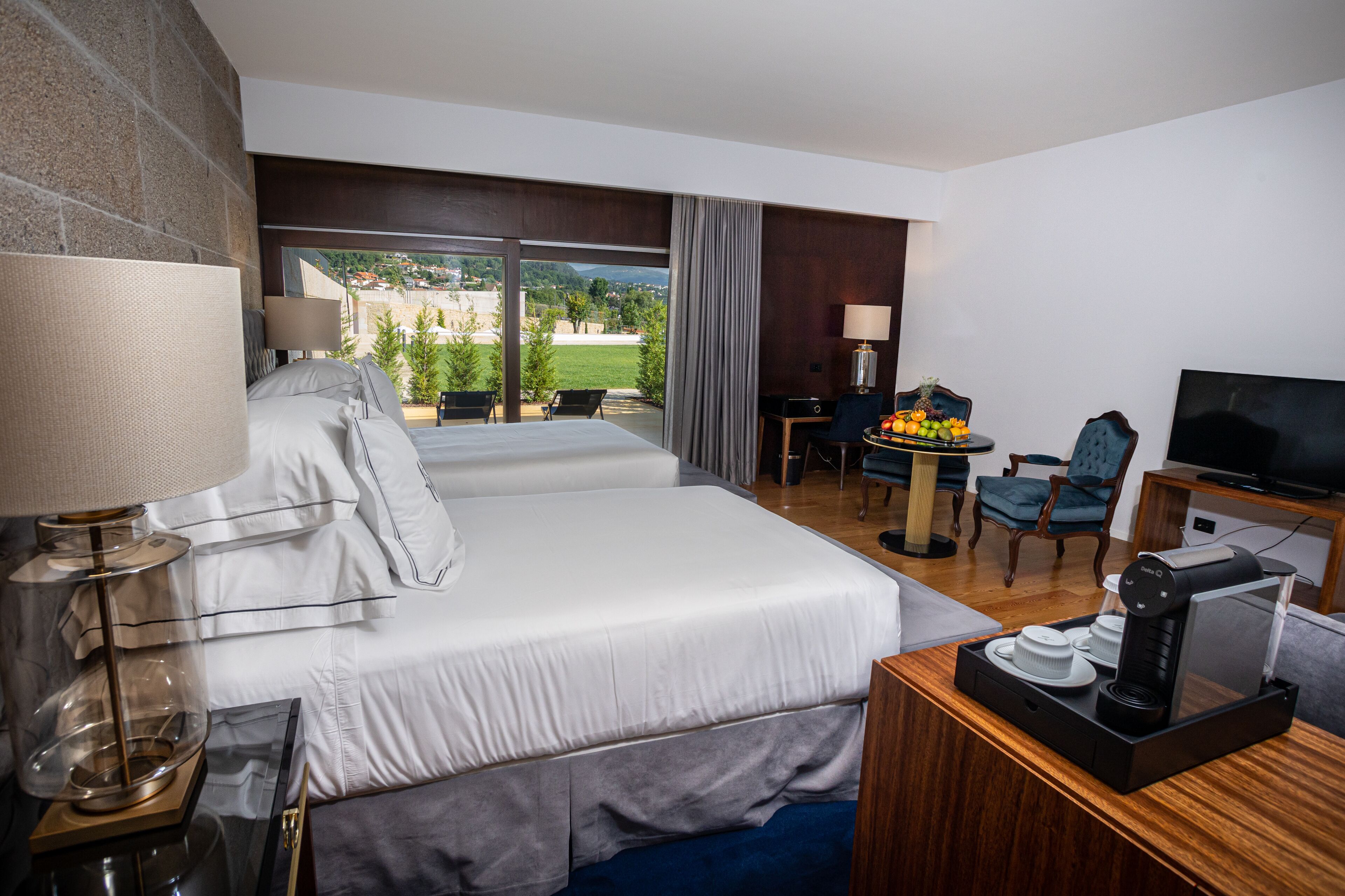 A hotel room with a large bed, a desk with a coffee maker, a television, and a view of the outdoors.