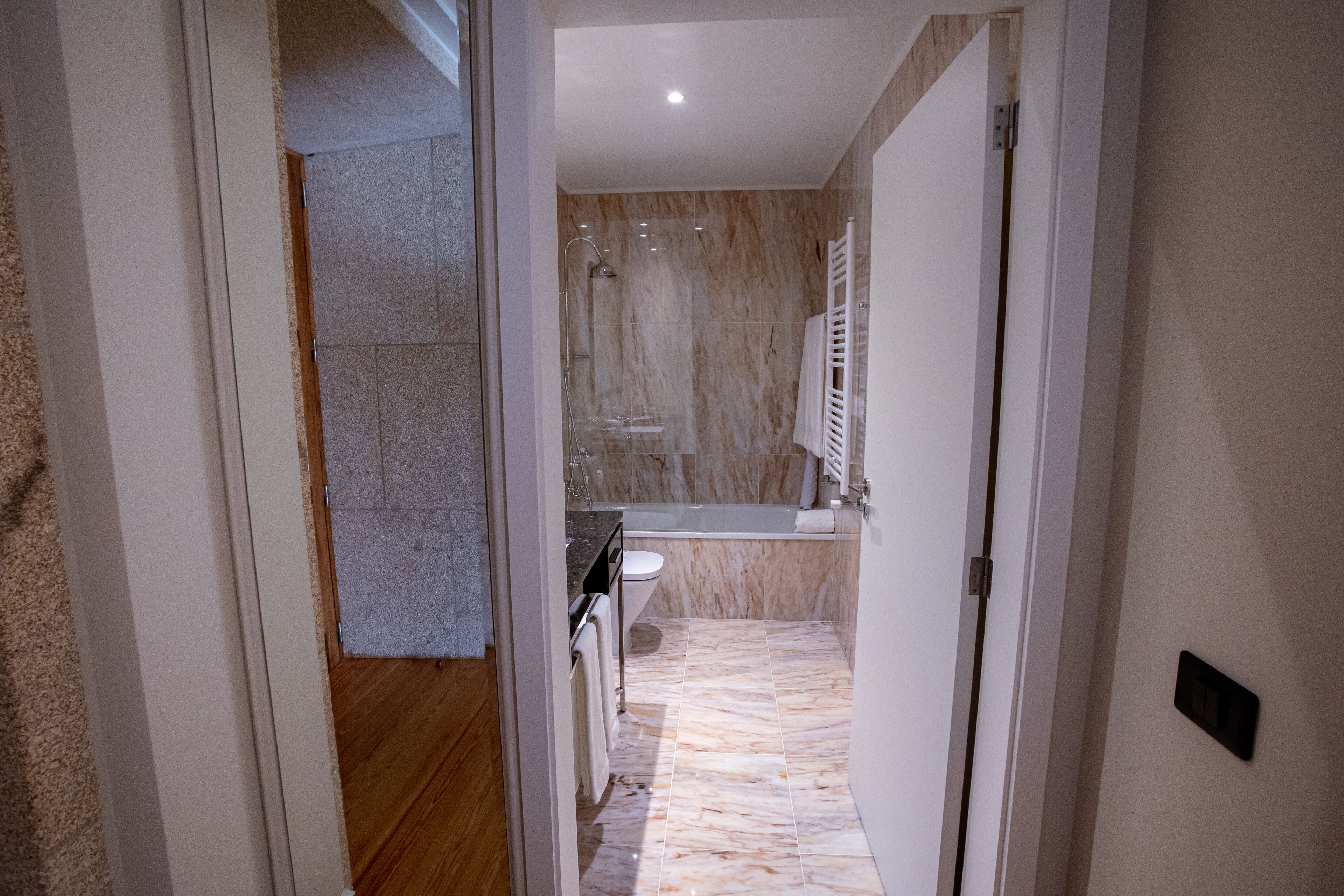 Un baño moderno con cabina de ducha de vidrio, suelo de mármol y lavamanos blanco.