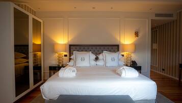 A large bed with white linens, two bedside tables with lamps, a wardrobe, and a mirror.