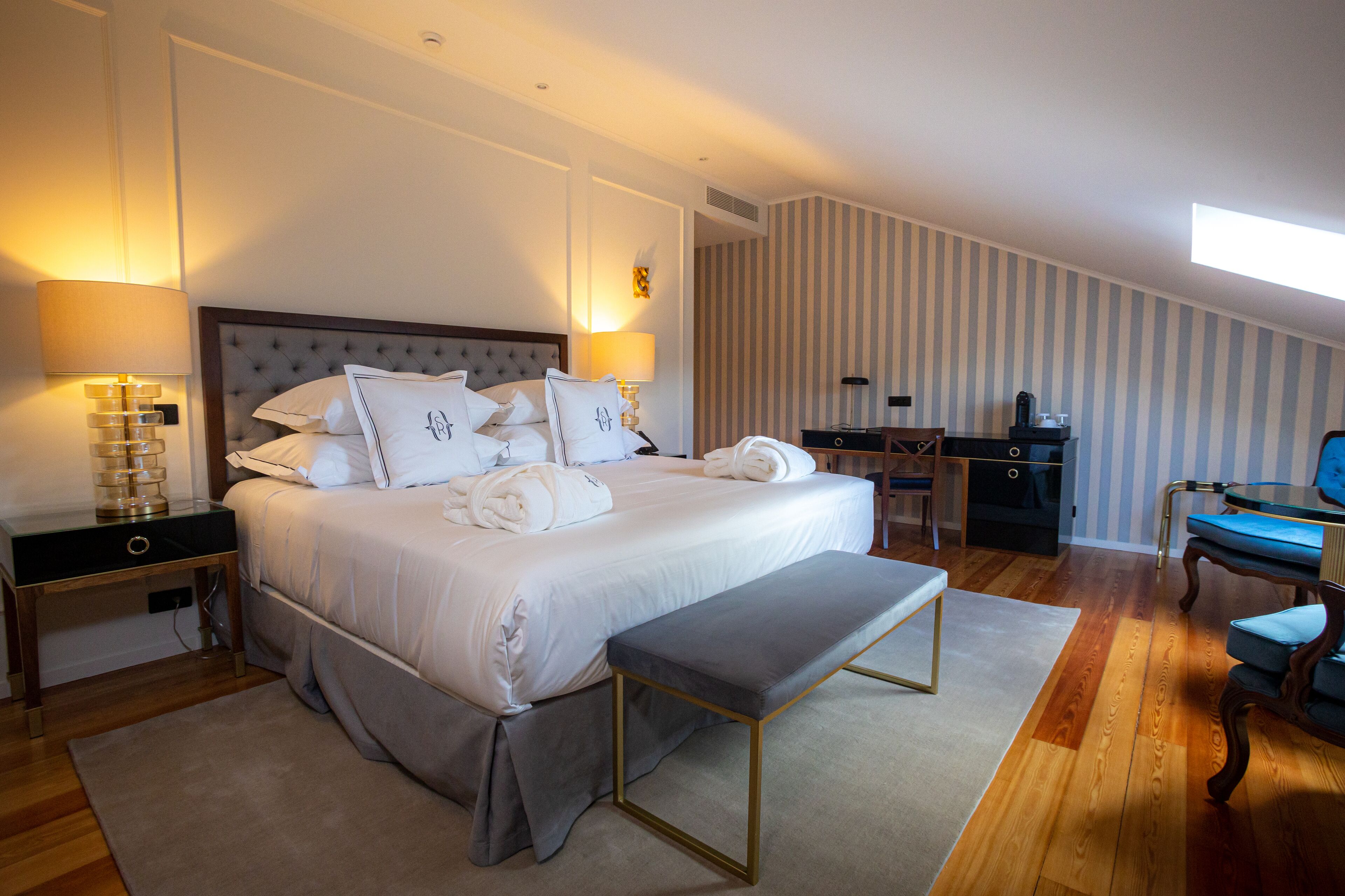 A modern bedroom with a large bed, bedside lamps, a bench, a desk, and a chair.