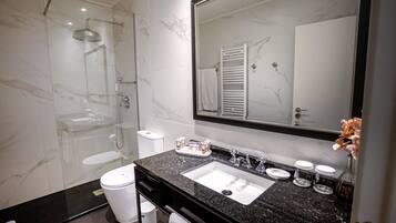 A modern bathroom with a glass-enclosed shower, a white toilet, a black granite sink, and a large mirror.