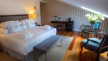 A hotel room with a large bed, a desk, a chair, a bench, and a small table with a vase of flowers.
