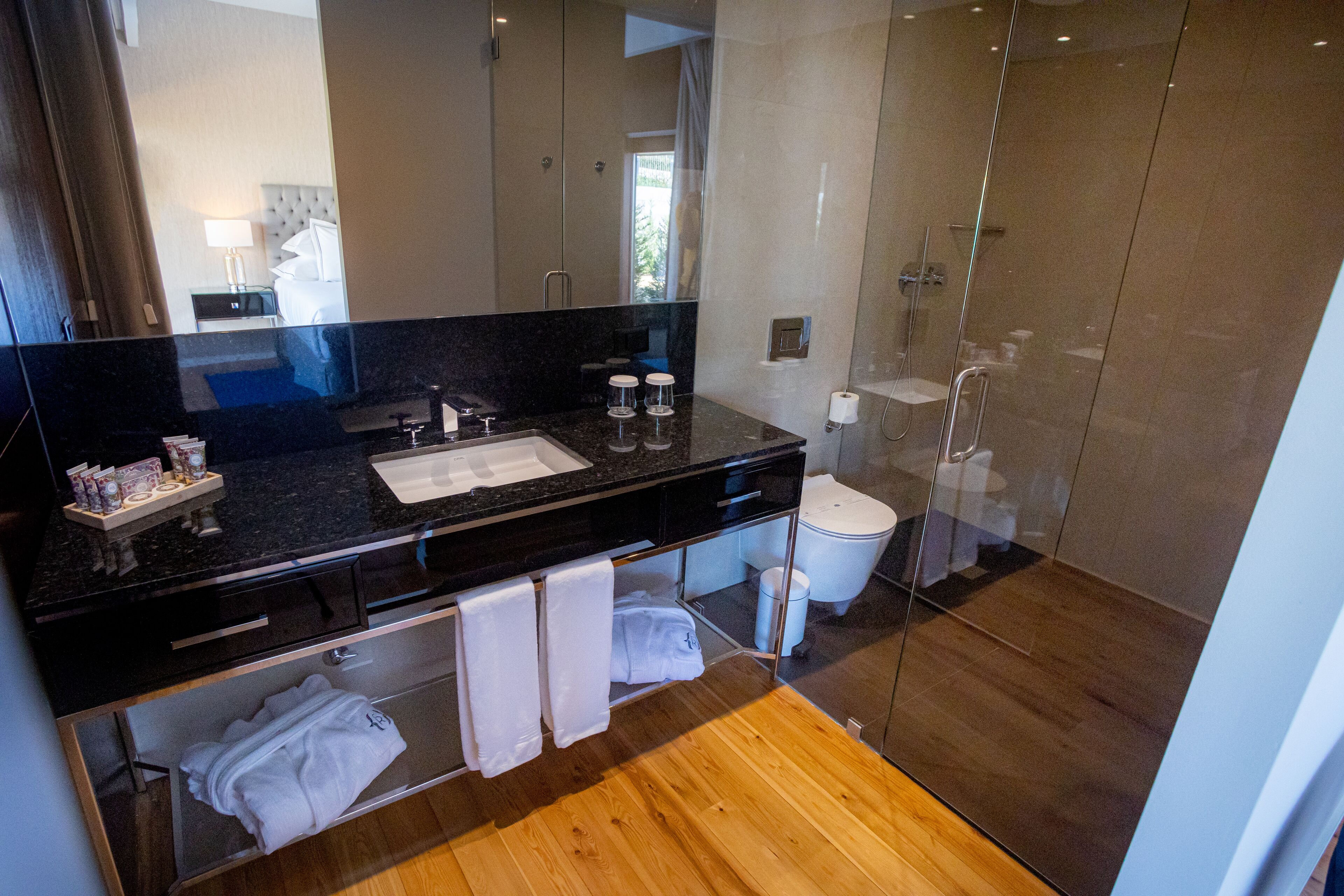 A modern bathroom with a black countertop, a glass shower enclosure, and a wooden floor.