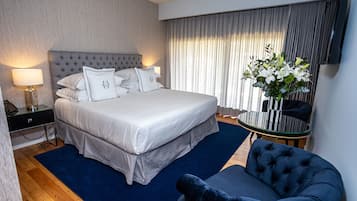 Habitación de hotel con una cama grande, una mesita de noche con lámpara, una mesa redonda y un sillón azul oscuro.