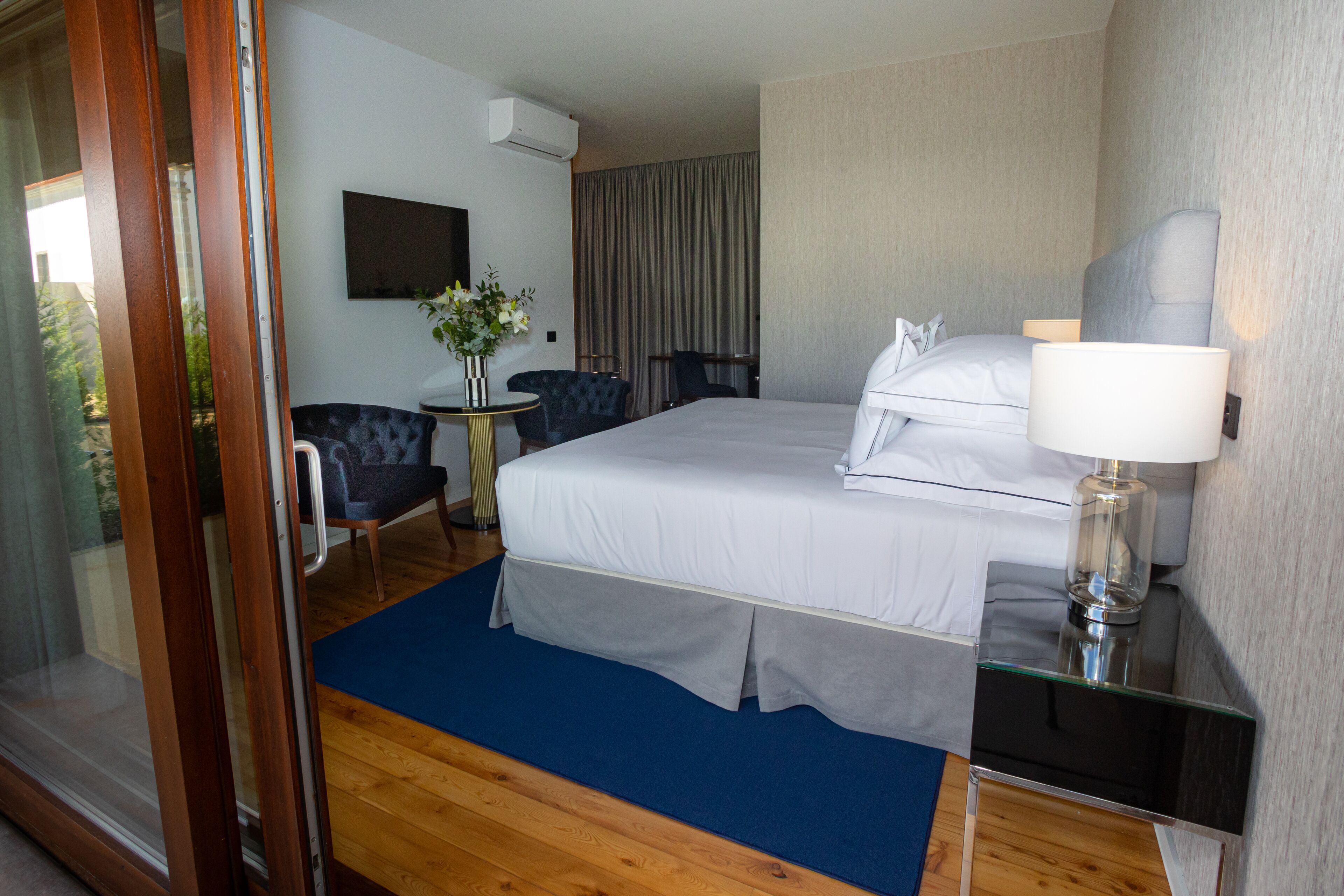 Habitación de hotel con cama, escritorio, silla, lámpara y vistas al exterior.