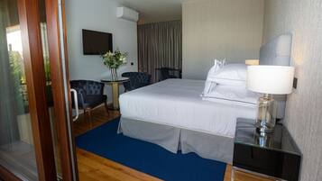 Habitación de hotel con cama, escritorio, silla, lámpara y vistas al exterior.