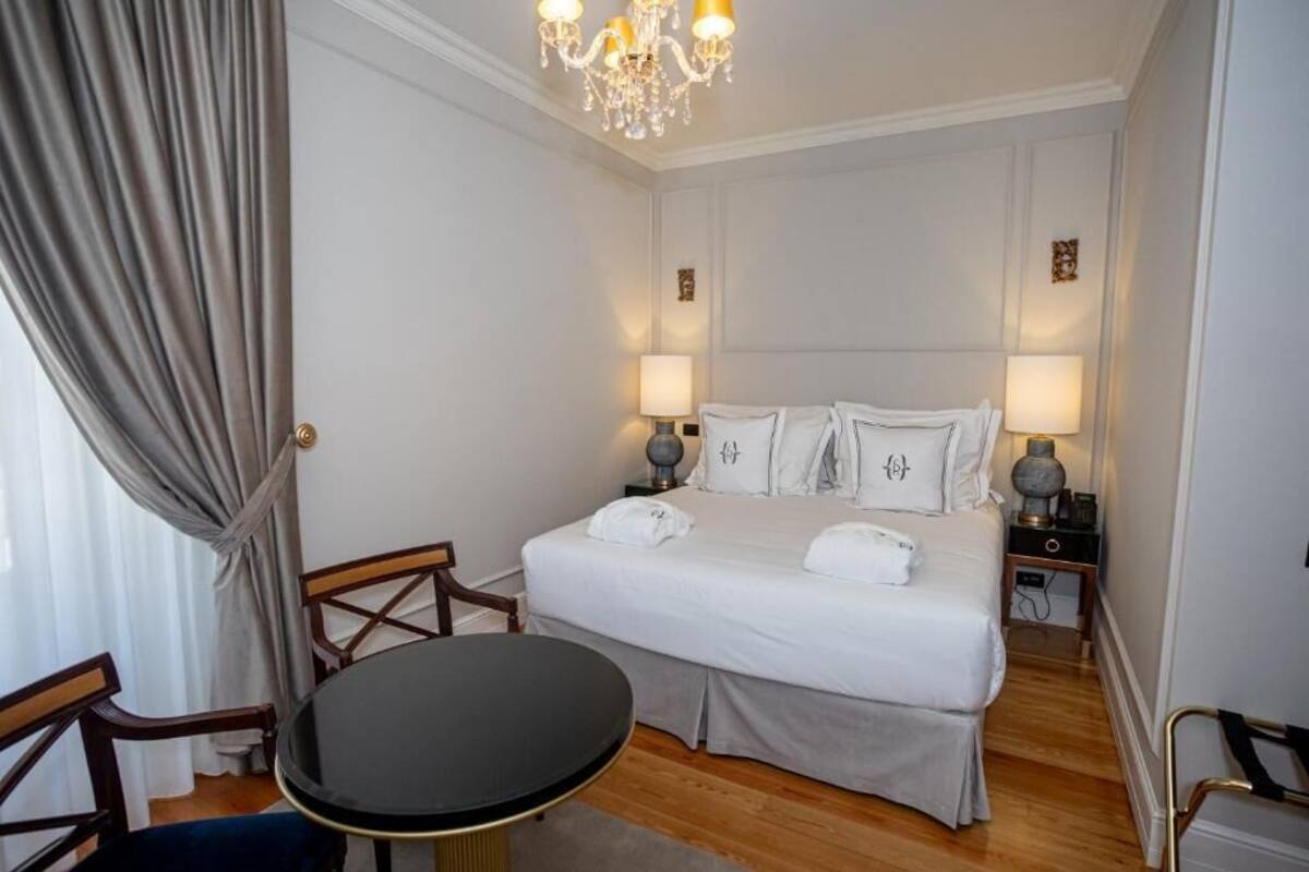 A hotel room with a bed, two bedside tables, a chandelier, a round table, and a chair.