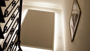 Un escalier surmonté d’une fenêtre en verre, un luminaire fixé au mur et un tableau encadré.