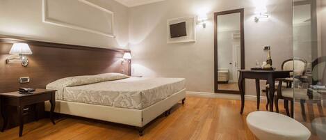 A hotel room with a bed, bedside table, lamp, and a small desk with a chair.