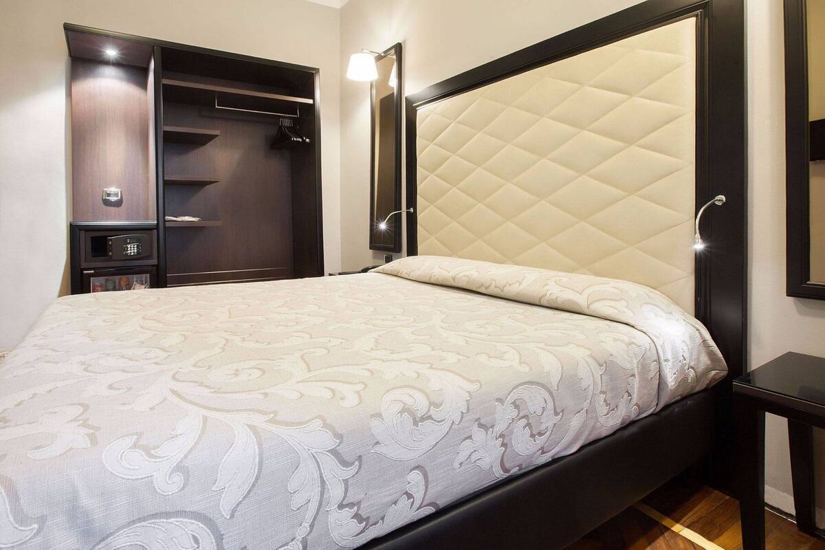 A hotel room with a bed, a wardrobe, a mirror, and a bedside table.