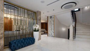 A spacious lobby with a marble floor, a blue bench, a large white vase with flowers, and a staircase with a wooden railing. - Gleam Collection Hotel (Istanbul)