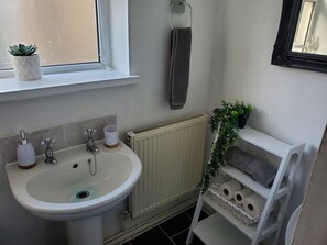 A bathroom with a sink, two faucets, a towel rack, a radiator, and a shelf with towels and a plant.