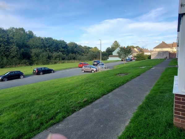 A residential street with parked cars, a sidewalk, and houses in the background.