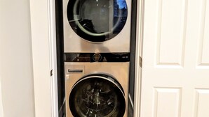 Une petite buanderie équipée d’un lave-linge à chargement par le haut et d’un sèche-linge à chargement frontal, le tout dissimulé derrière des portes blanches.