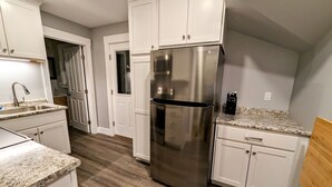 Une cuisine moderne avec des meubles blancs, un réfrigérateur en acier inoxydable, des plans de travail en granit et un plancher en bois.