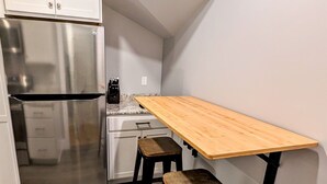 Une cuisine de taille réduite, dotée d’un réfrigérateur en acier inoxydable, d’une table en bois et de deux tabourets.