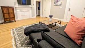 Un salon comprenant un canapé, une table basse, un meuble, un téléviseur à écran plat et une porte donnant sur une autre pièce.
