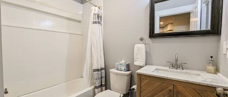 A bathroom with a bathtub, toilet, and vanity with a mirror.