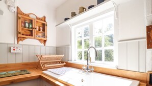 A kitchen with a wooden countertop, a built-in sink, a window with a view of greenery, and a wooden cabinet above the sink. - Warren Cottage (Bures)