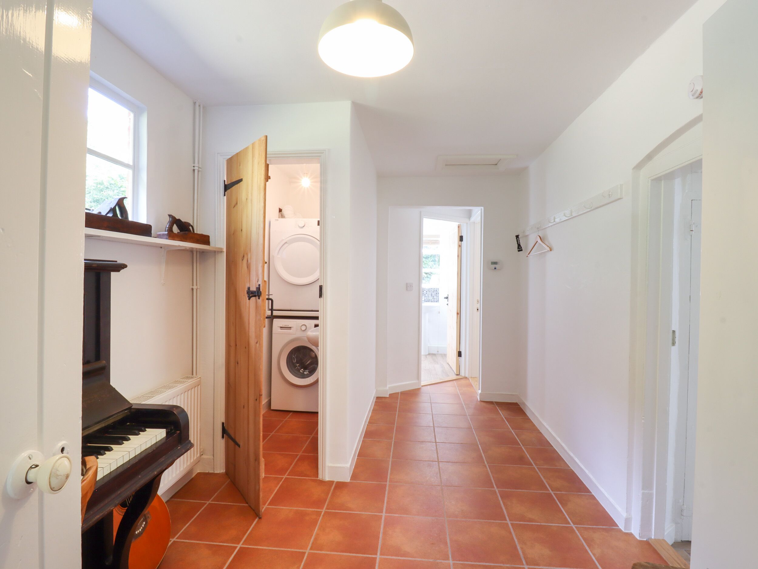 Un pasillo con un piano, una lavadora y una puerta que da a otra habitación.