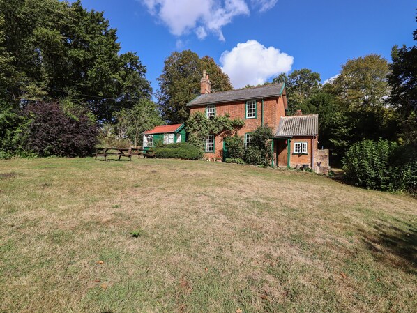A large brick house with a red roof, surrounded by a grassy lawn and trees. - Warren Cottage (Bures)