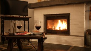 Une pièce chaleureuse avec une cheminée, un téléviseur et une table où sont disposés des verres à vin et de la nourriture.