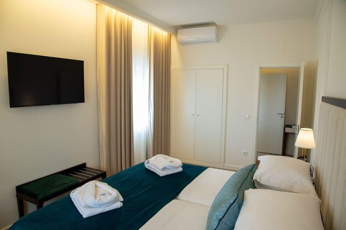Quarto de hotel com uma cama, televisão fixada na parede, guarda-roupa e espelho.
