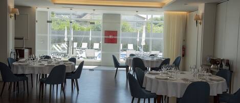 A dining area with round tables set for a meal, chairs, and a view of the outdoors.