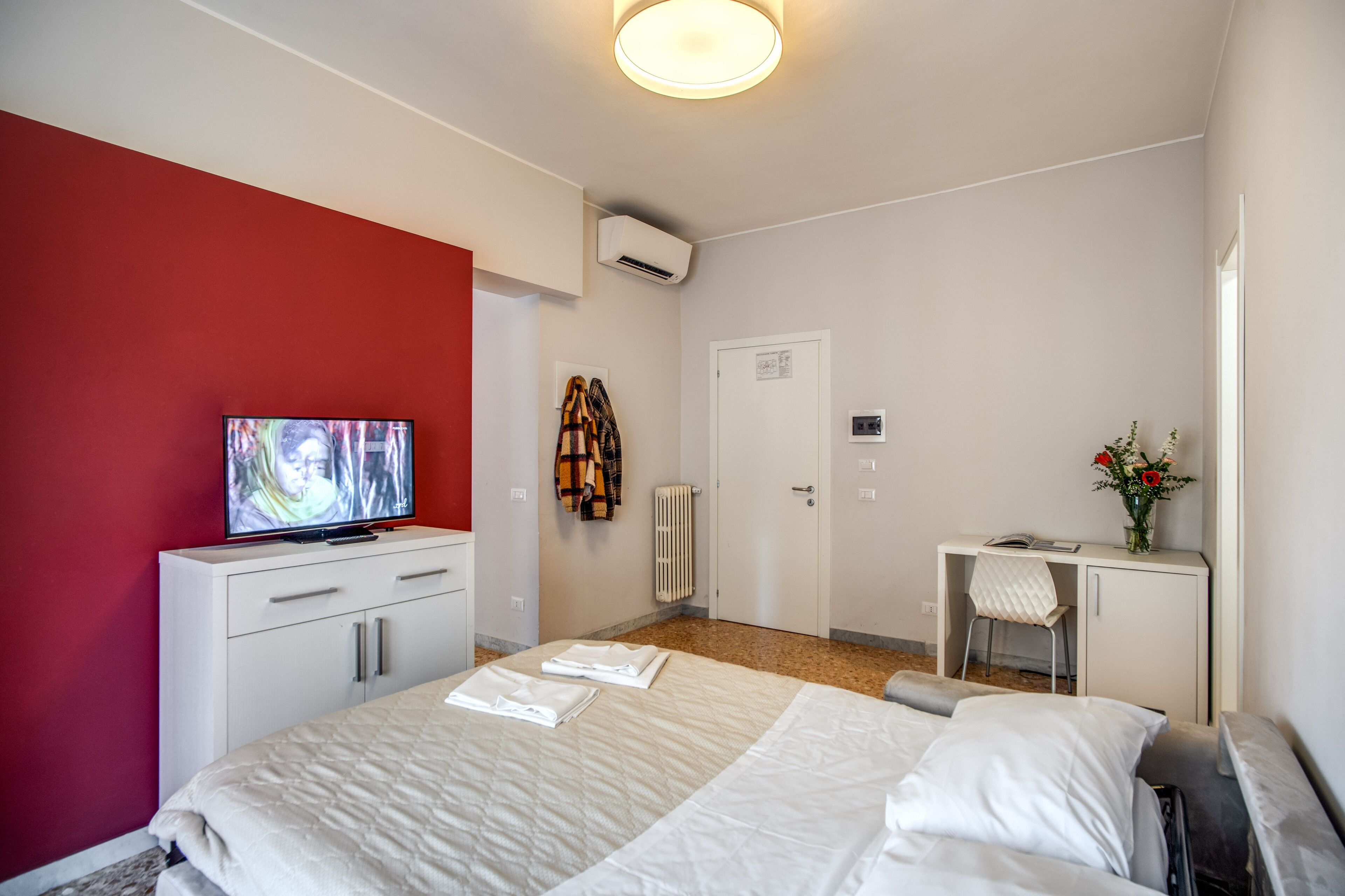 A hotel room with a bed, a desk, a chair, a television, and a radiator.