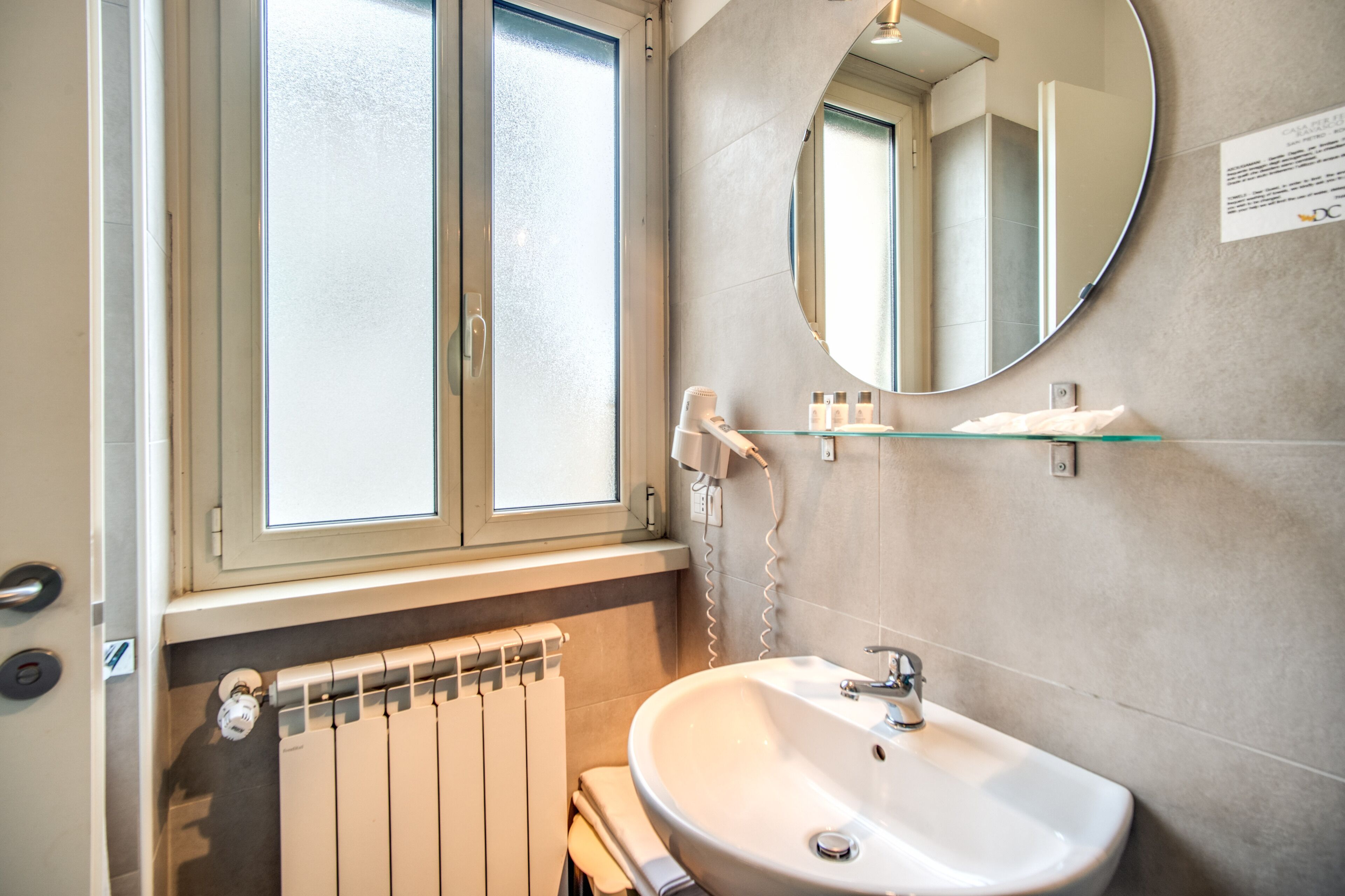 A bathroom with a white sink, a round mirror, and a window with frosted glass.