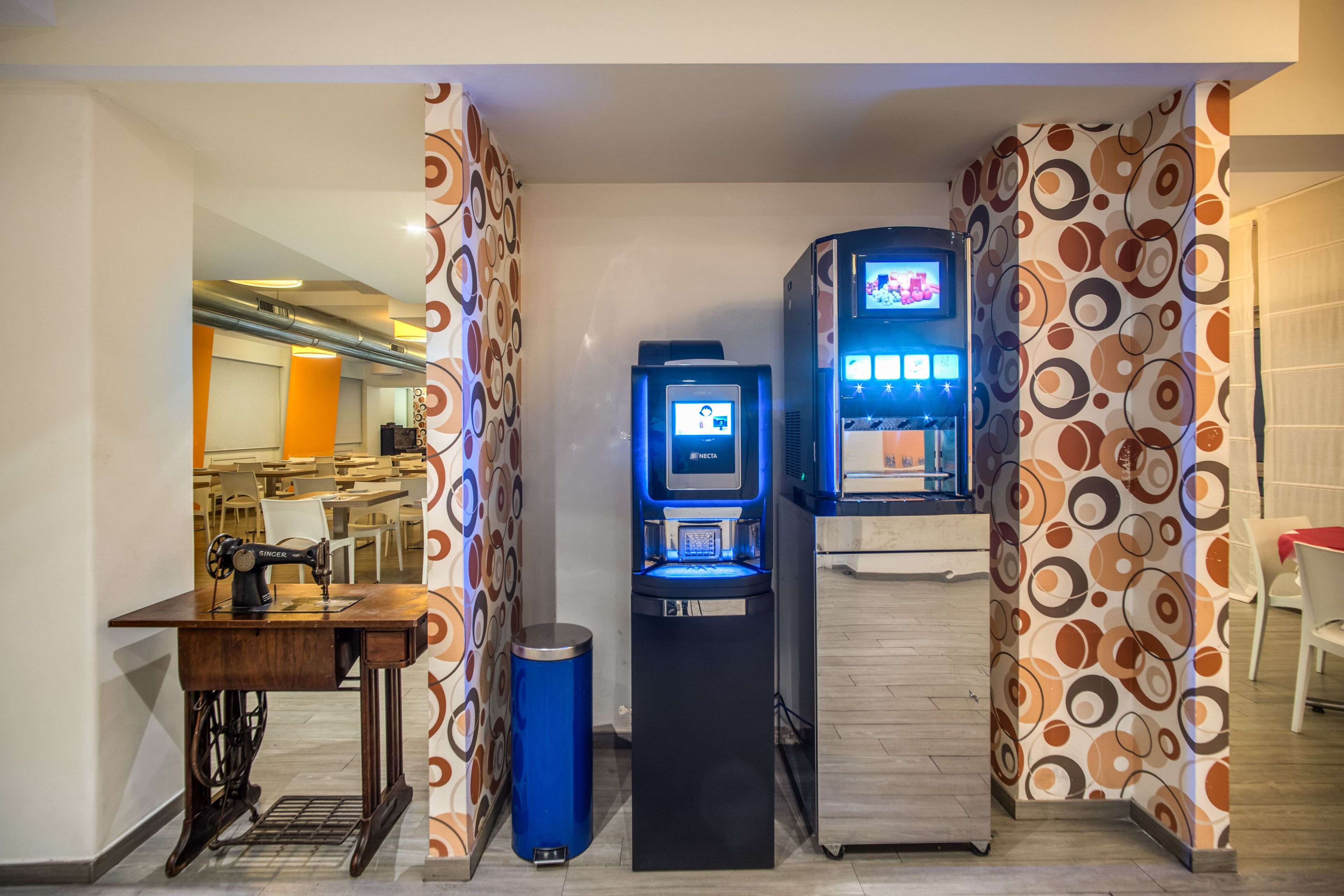 A room with a sewing machine, a blue trash bin, and a digital kiosk with a screen.