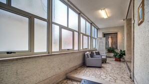 A hallway with large windows, a stone floor, a sofa, and a statue. - Casa Per Ferie Ravasco San Pietro (Rome)