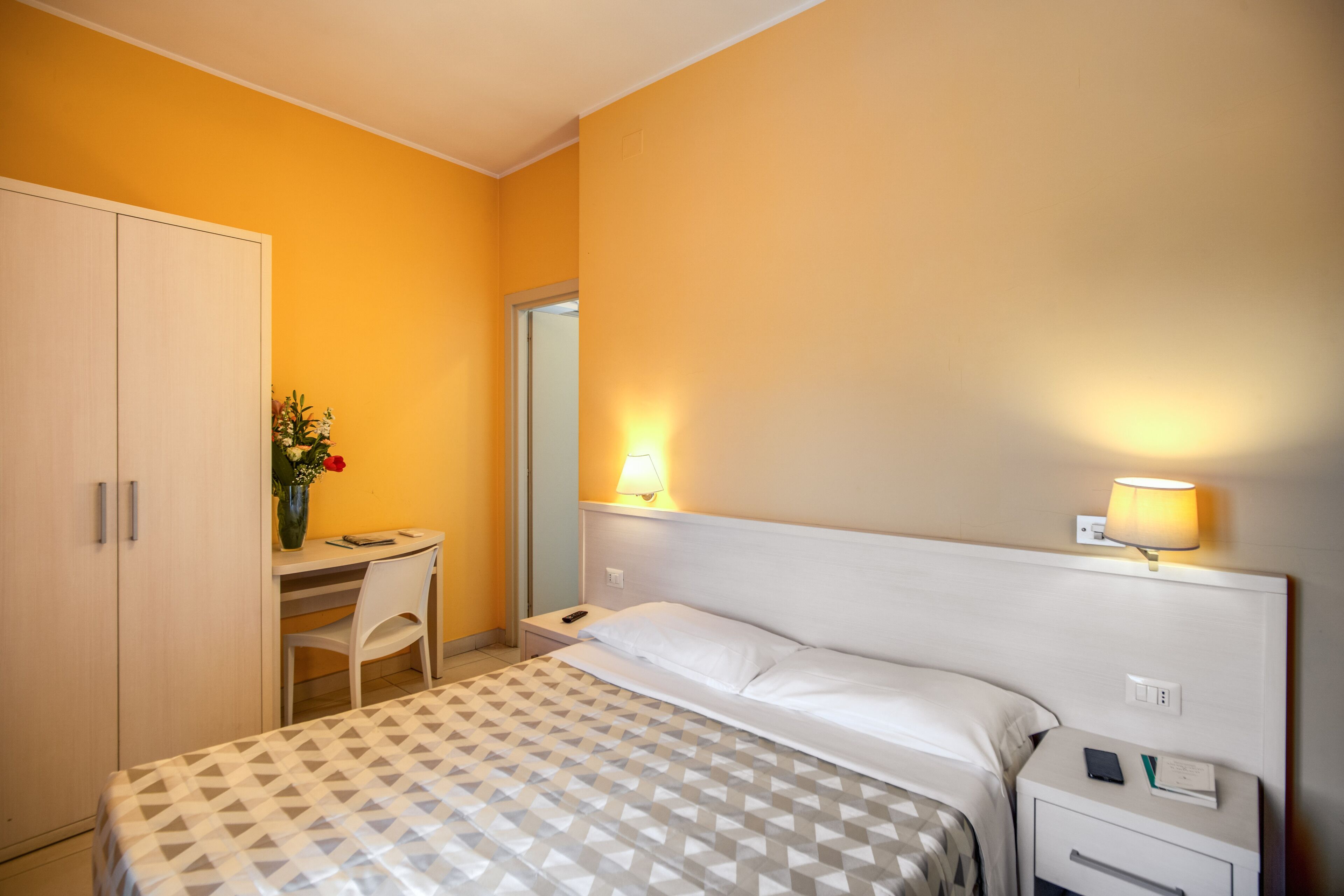 Une chambre d’hôtel avec un lit, un bureau, une chaise et une armoire.