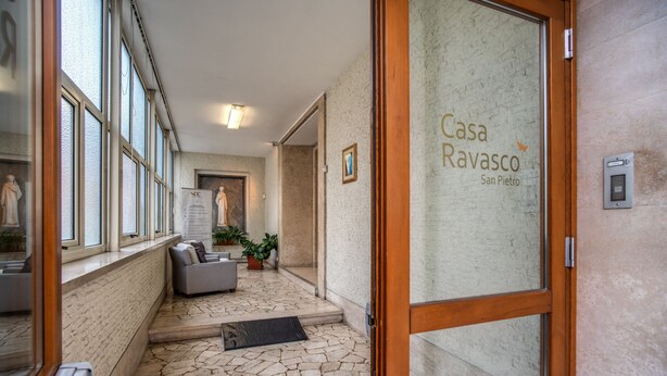 A hotel entrance with a stone-tiled floor, a reception desk, and a seating area with a sofa and plants. - Casa Per Ferie Ravasco San Pietro (Rome)